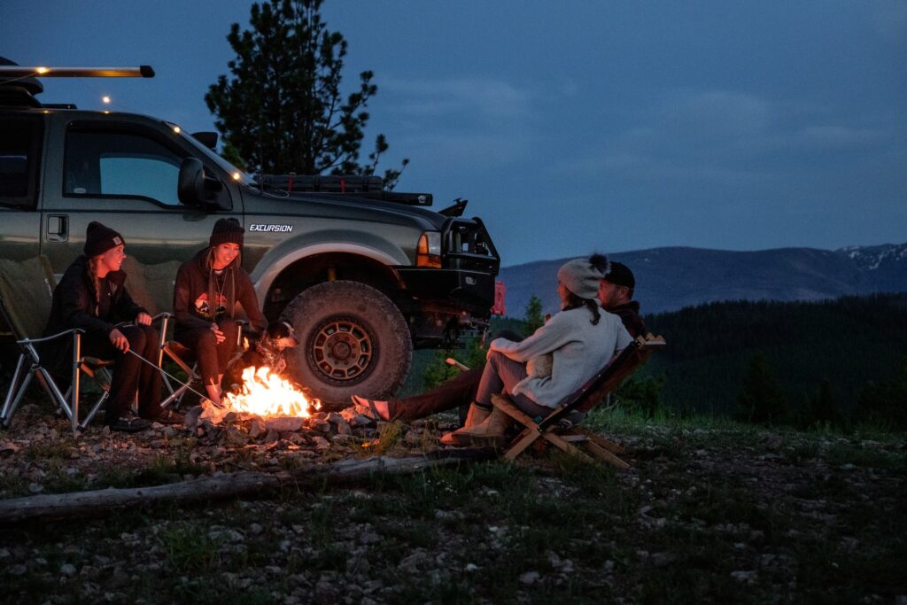 Overland vehicle - group gathered around a campfire near their overland vehicle