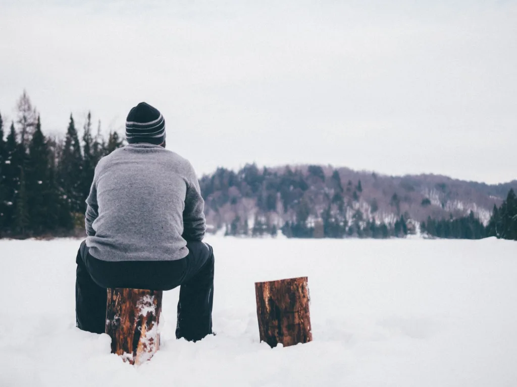 Peaceful man sitting on a log in a snow covered field.